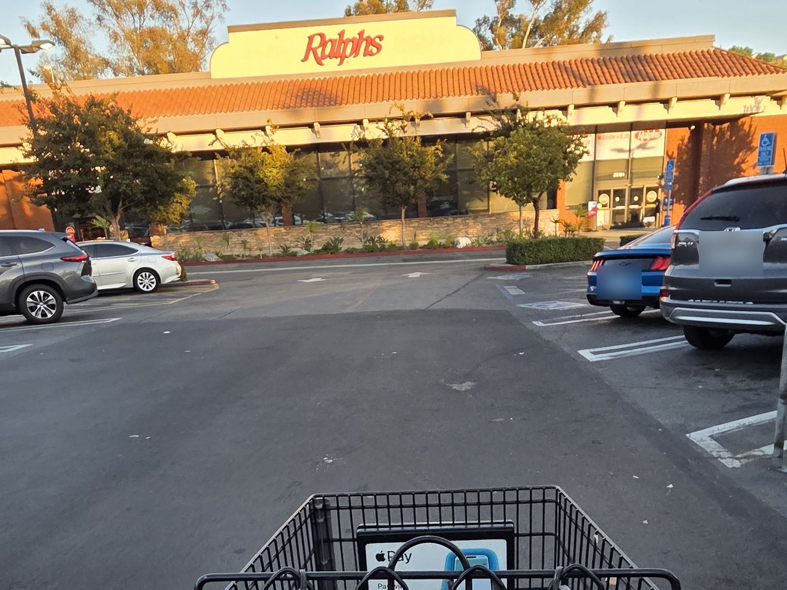 View from behind an empty shopping cart in a Ralphs parking lot at sunset, looking toward the store entrance.